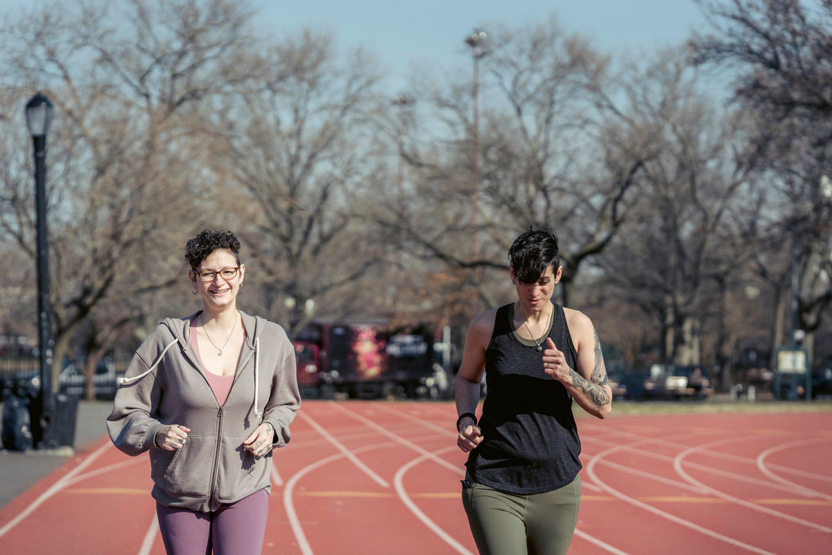 Smiling sportswomen running on track in sunlight